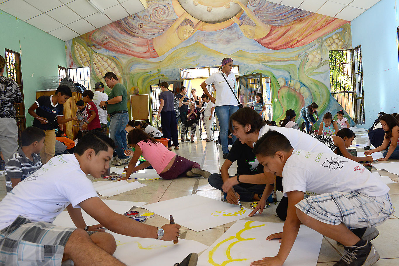 Mehrere Kinder und Jugendliche malen auf großen Papieren auf dem Boden.