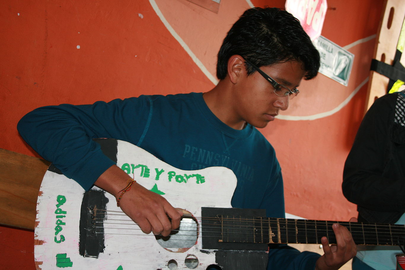 Ein Jugendlicher von CEPALC sitzt und spielt auf der Gitarre.
