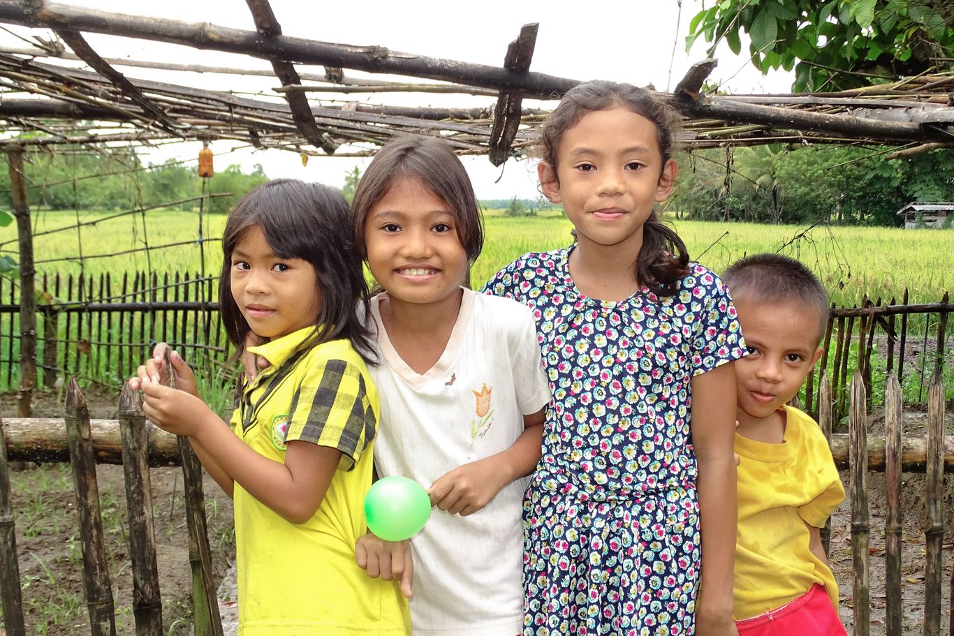 Vier Kinder stehen vor einem Zaun und lächeln in die Kamera.
