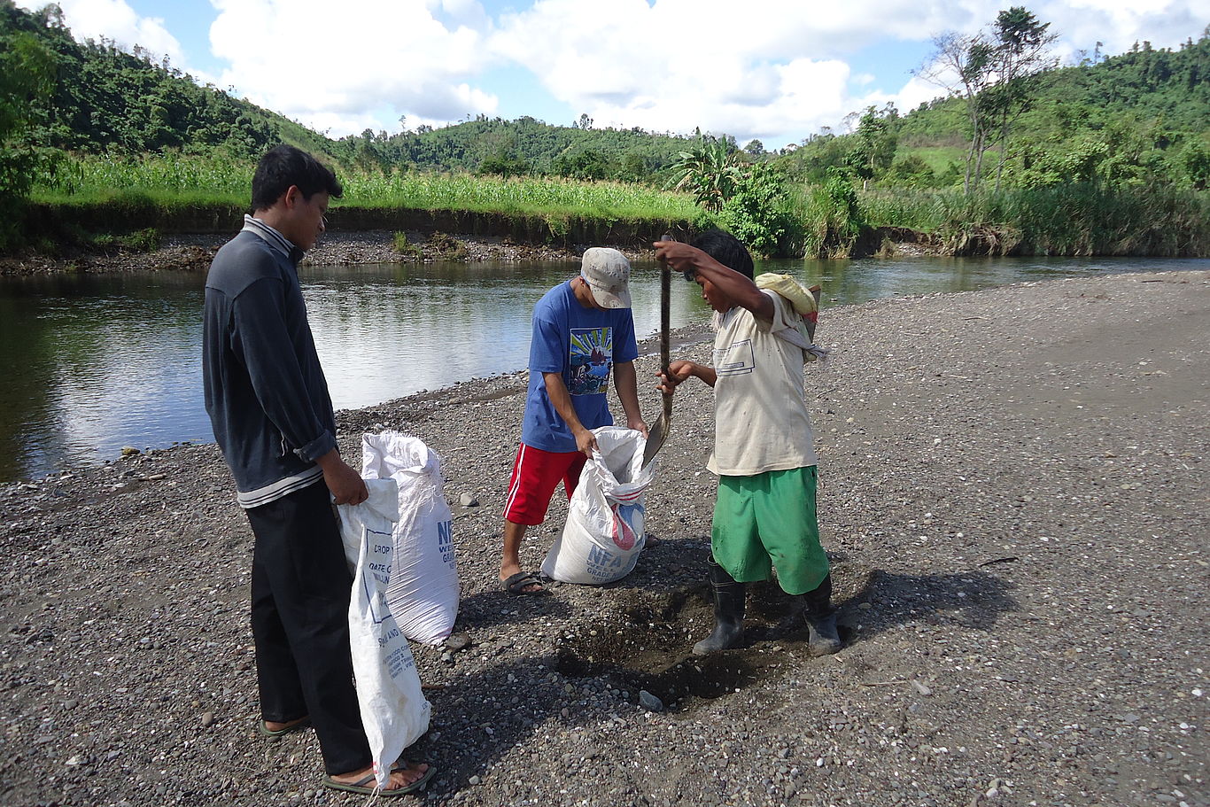 Flussbeet in Davao Drei Männer befüllen Säcke mit Kies eines Flussbetts.