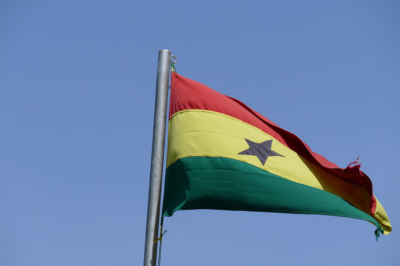 Foto: Sebastian Poltschak Ghanaische Flagge mit rot-gelb-grünen Querstreifen und Stern in der Mitte vor blauem Himmel.