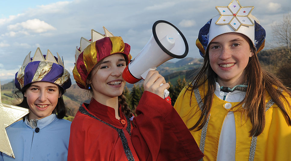 Drei Sternsinger/innen schauen in die Kamera, eine hat ein Megaphon