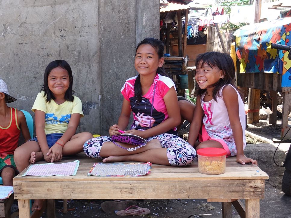 Drei philippinische Kinder sitzen auf einem Tisch, lachen und scherzen