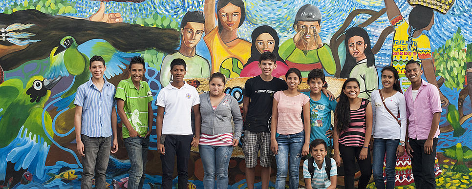 a group of teenagers standing in front of a mural painting