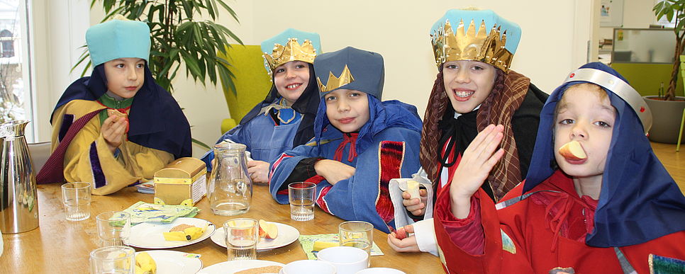 Sternsinger/innen zu Besuch Fünf Sternsinger/innen sitzen am Essentisch bei Äpfel und Keksen..