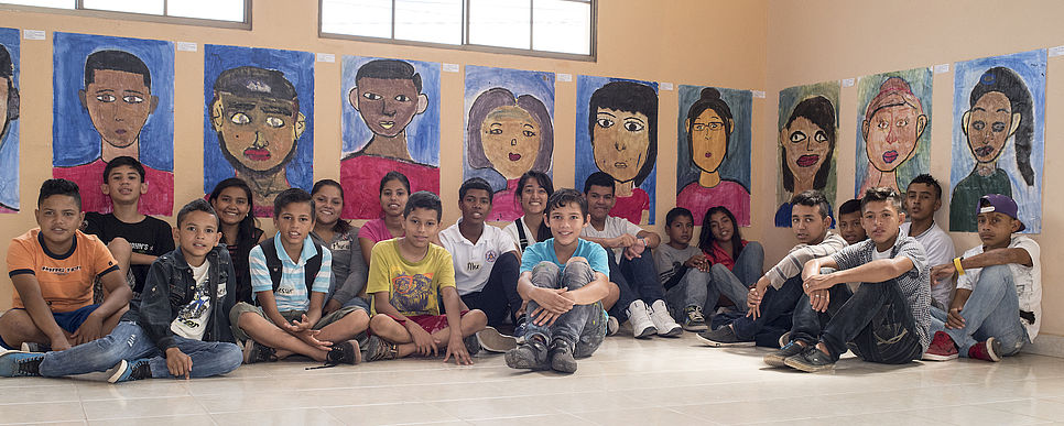 Kinder sitzen vor ihren selbstgemalten Portraits
