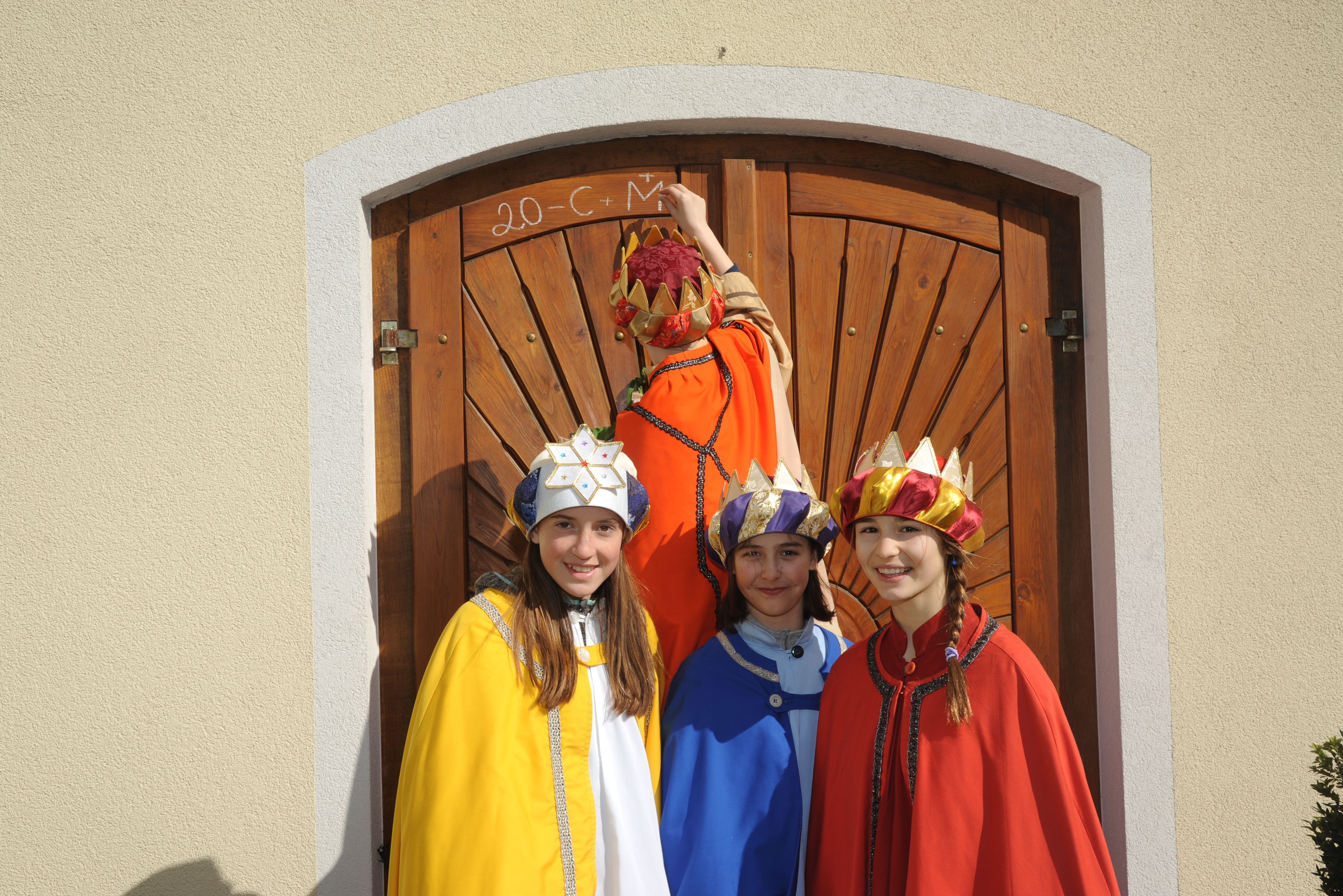 Vier Kinder, gekleidet als die heiligen drei Könige samt Sternsinger, schreiben an eine Tür.