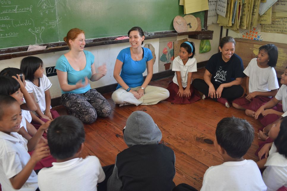 LernEinsatzteilnehmerinnen sitzen mit philippinischen Kindern in einer Klasse und erzählen. 