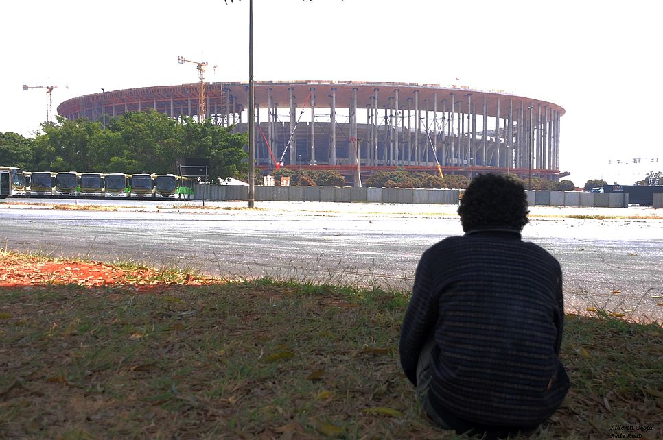 Ein Jugendlicher sitzt vor dem halbgebauten Stadion von Rio.
