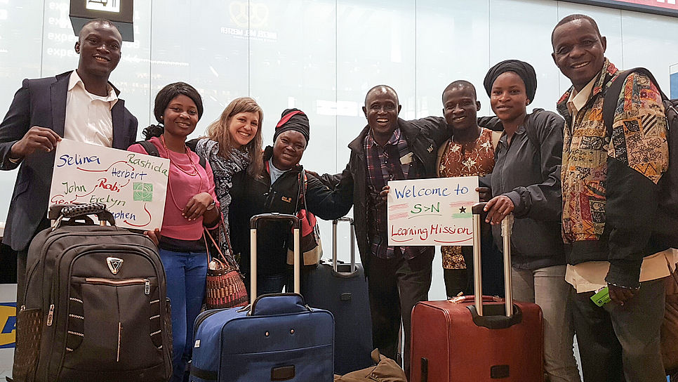Besucher und Besucherinnen aus Ghana lächeln bei der Ankunft in die Kamera.