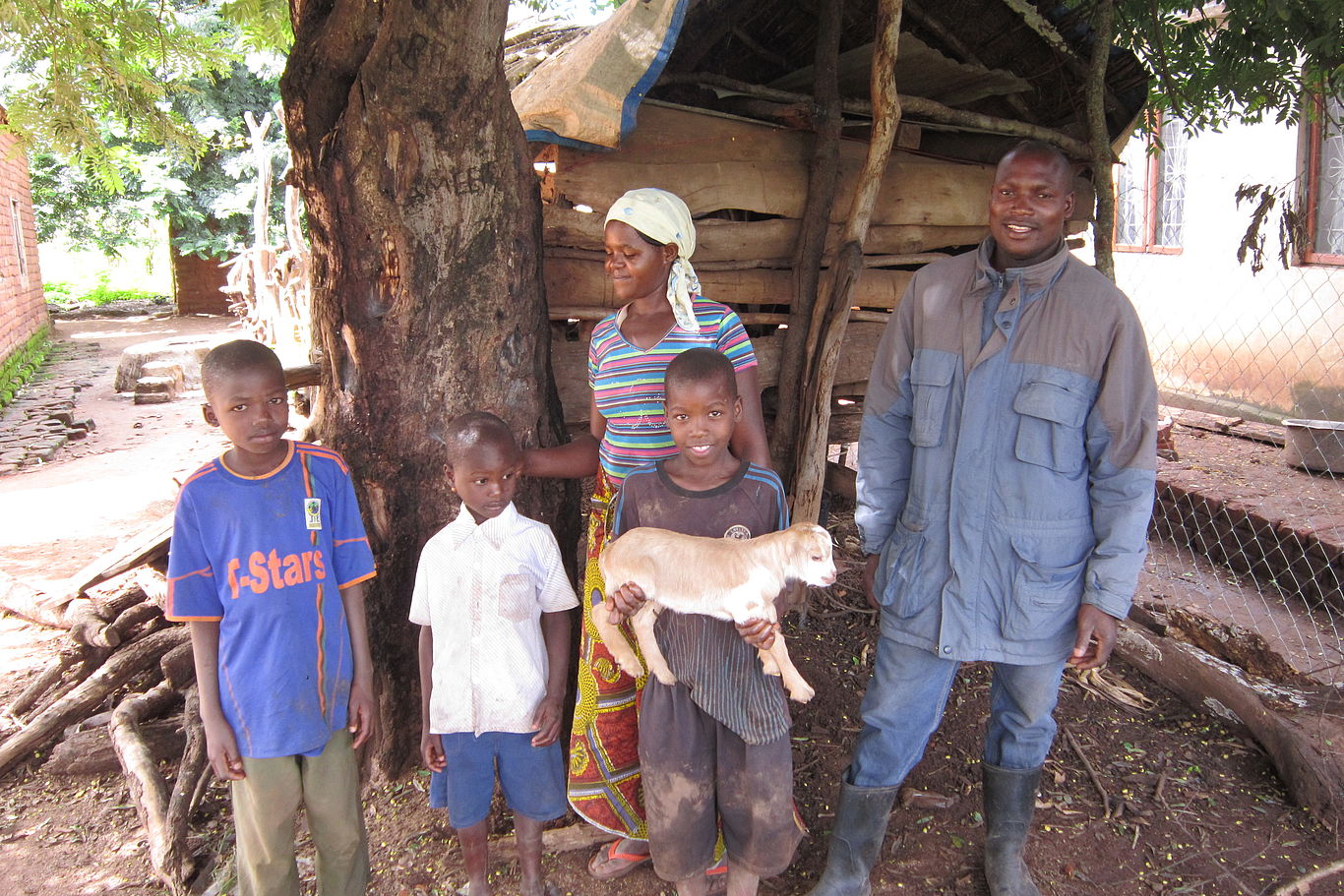 Eine Familie steht unter einem Baum und ein Junge hält ein Kitz auf den Armen.