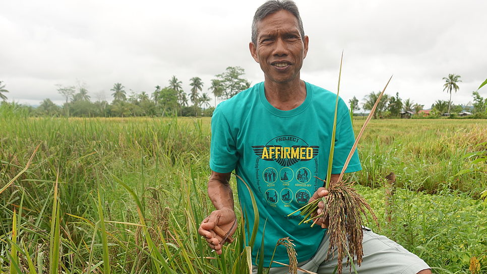 Ein Bauer auf einem Reisfeld mit einer Reispflanze in der Hand.