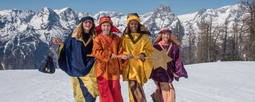 Sternsinger lachen in die Kamera, im Hintergrund sind schneebedeckte Berge.