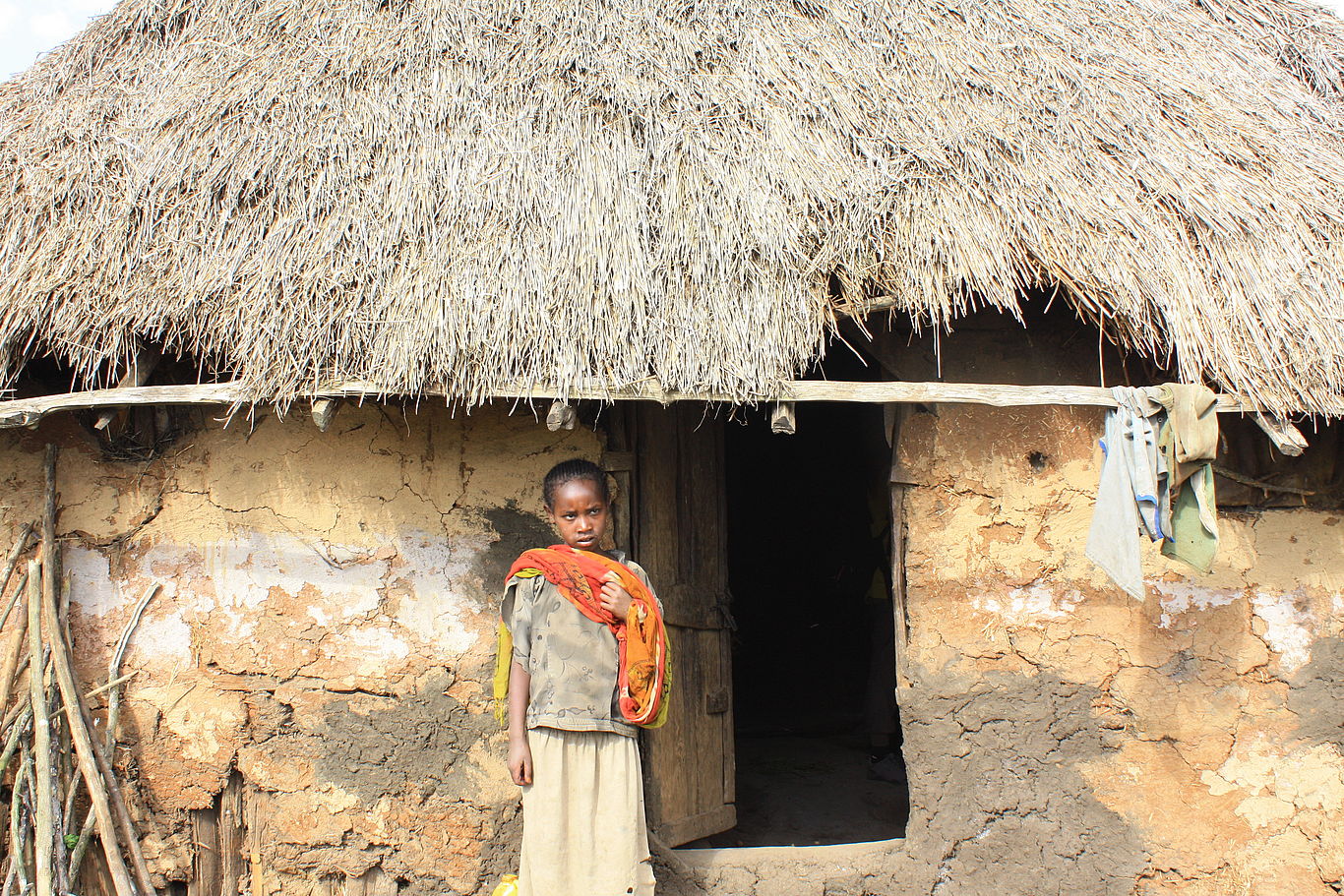 Ein Mädchen steht vor einer Lehmhütte mit Strohdach