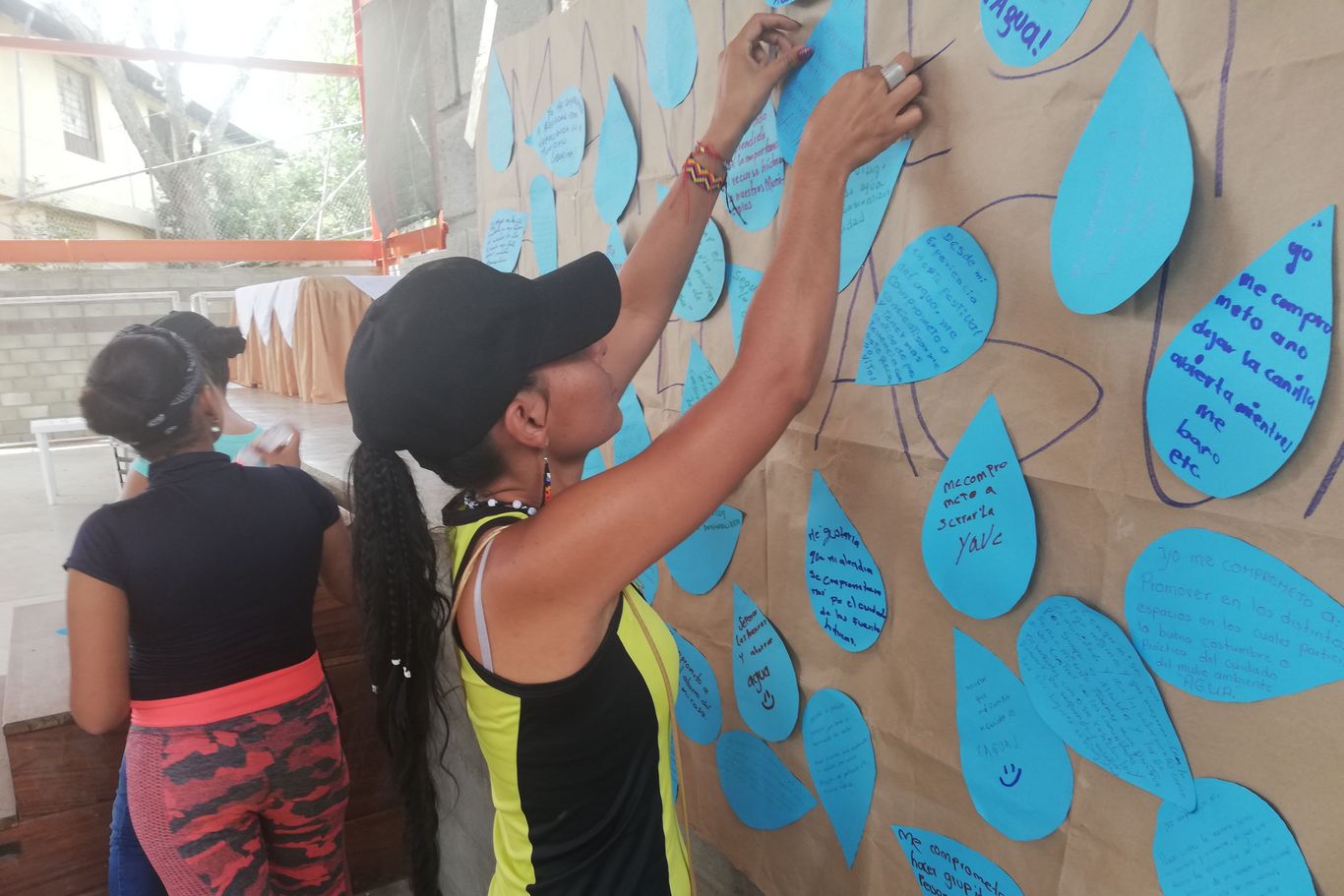 Verschiedenste Workshops und Dialoge zu Landrechte, Wasser- und Umweltschutz, Demokratie und Politik. Eine Frau hängt ein beschriebenes Papierblatt auf eine Wand zu vielen anderen dazu.