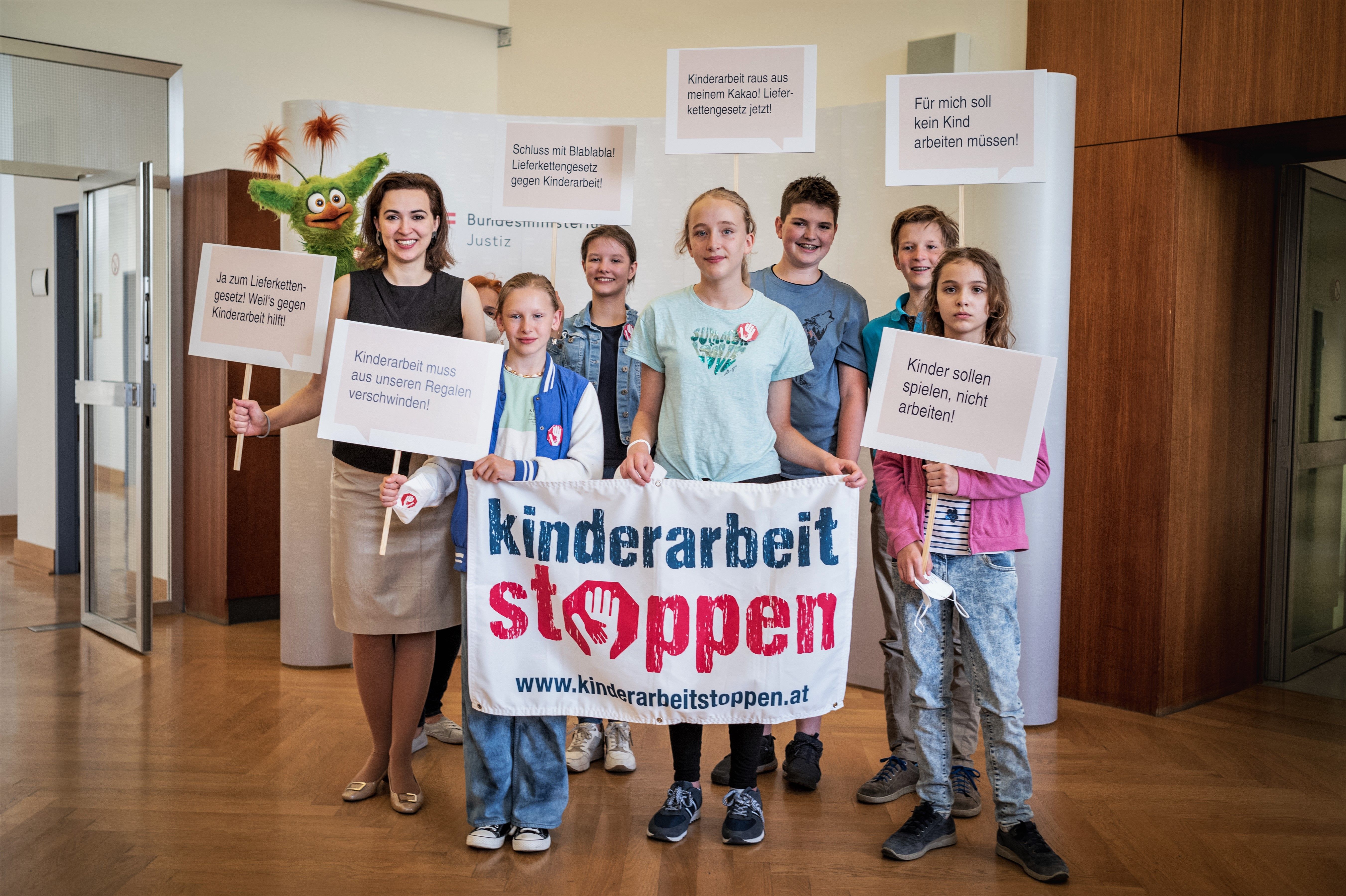 Sechs Kinder und BM Alma Zadic halten Transparent und Schilder mit der Forderung "Kinderarbeit stoppen!"