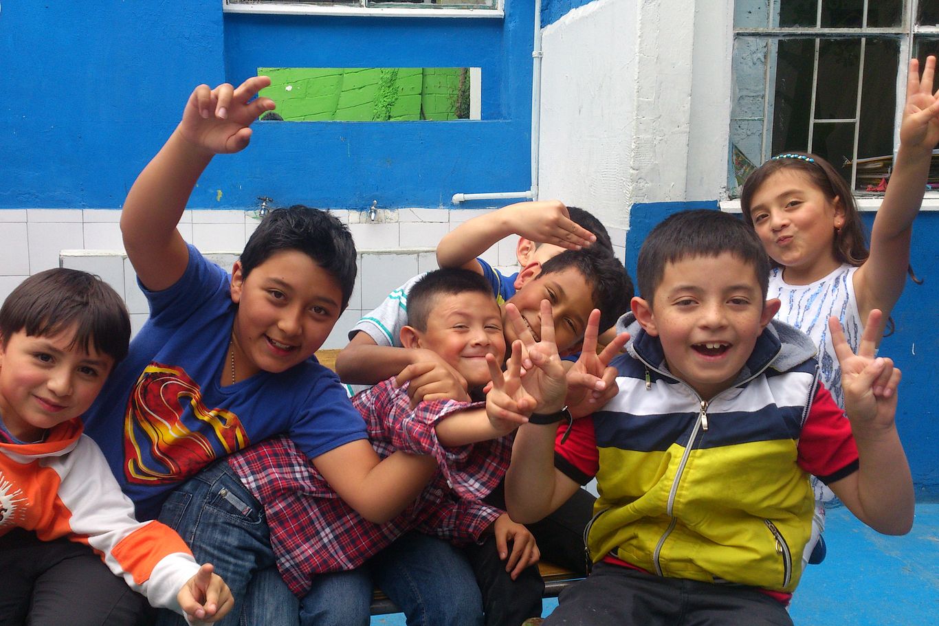 Kinder von CEPALC grinsen verschmitzt in die Kamera und zeigen das Peace-Zeichen