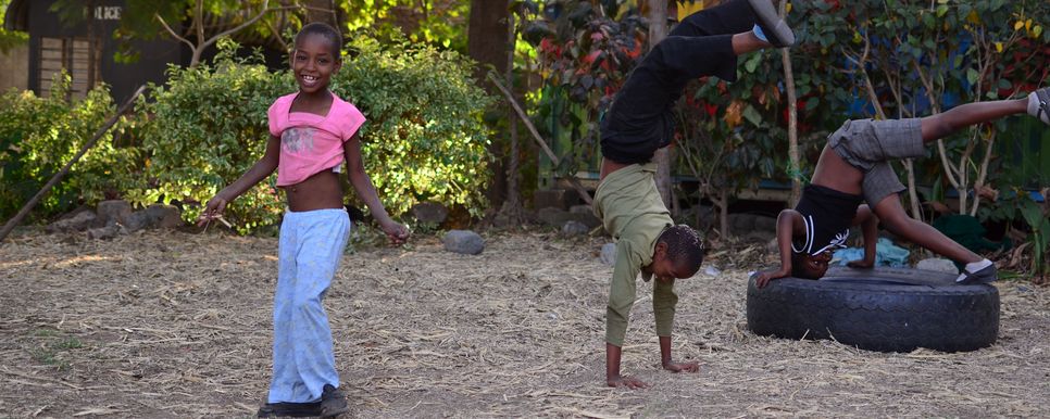 Drei Kinder betätigen sich akrobatisch auf einem grünen Hof.