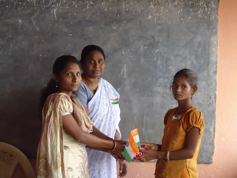 Eine Betreuerin übergibt zwei Schülerinnen ein Paket