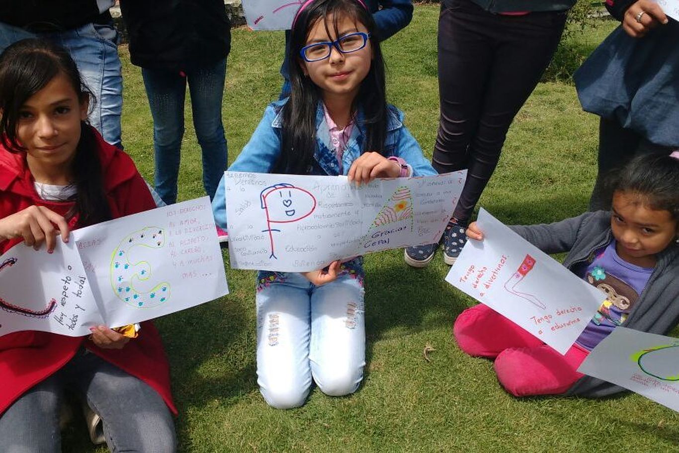 Mädchen zeigen Zeichnungen, die zusammengesetzt die Abkürzung CEPALC zeigen.