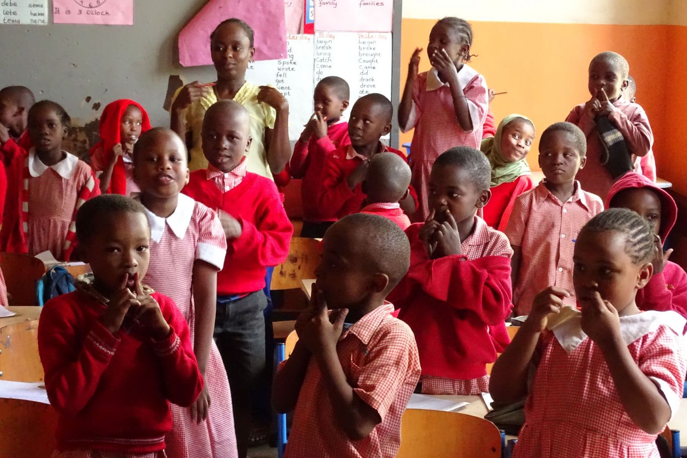 Kinder in roter Schuluniform stehen in einem Klassenraum von MPC.