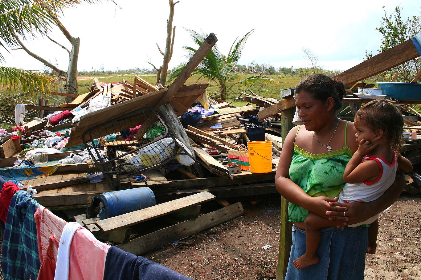 Eine Frau mit einem Kind am Arm steht vor einem durch Hurrikan zerstörten Haus.