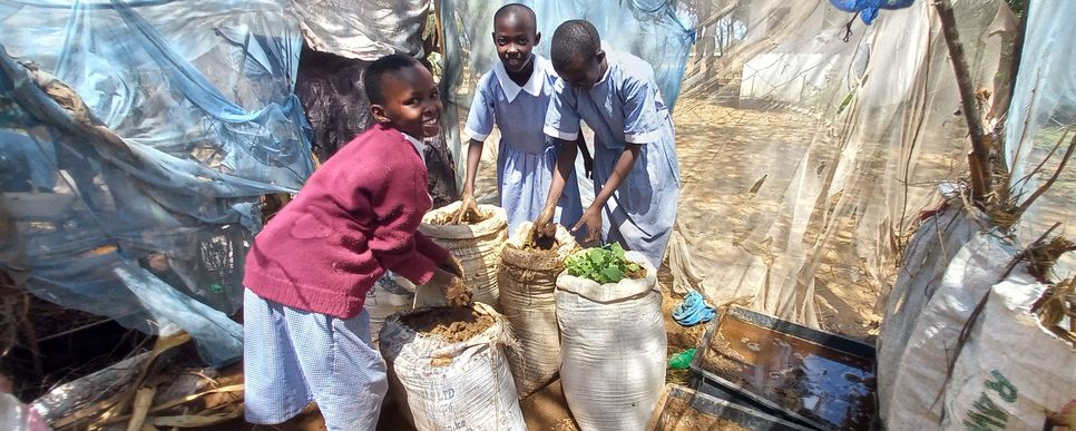 Kenianische Kinder haben Erde und Pflanzen in Säcken.