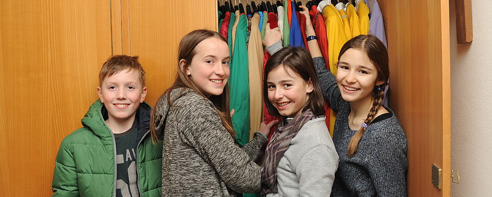 Drei Mädchen und ein Bub vor einem offenen Kleiderschrank mit Sternsingerkleidung