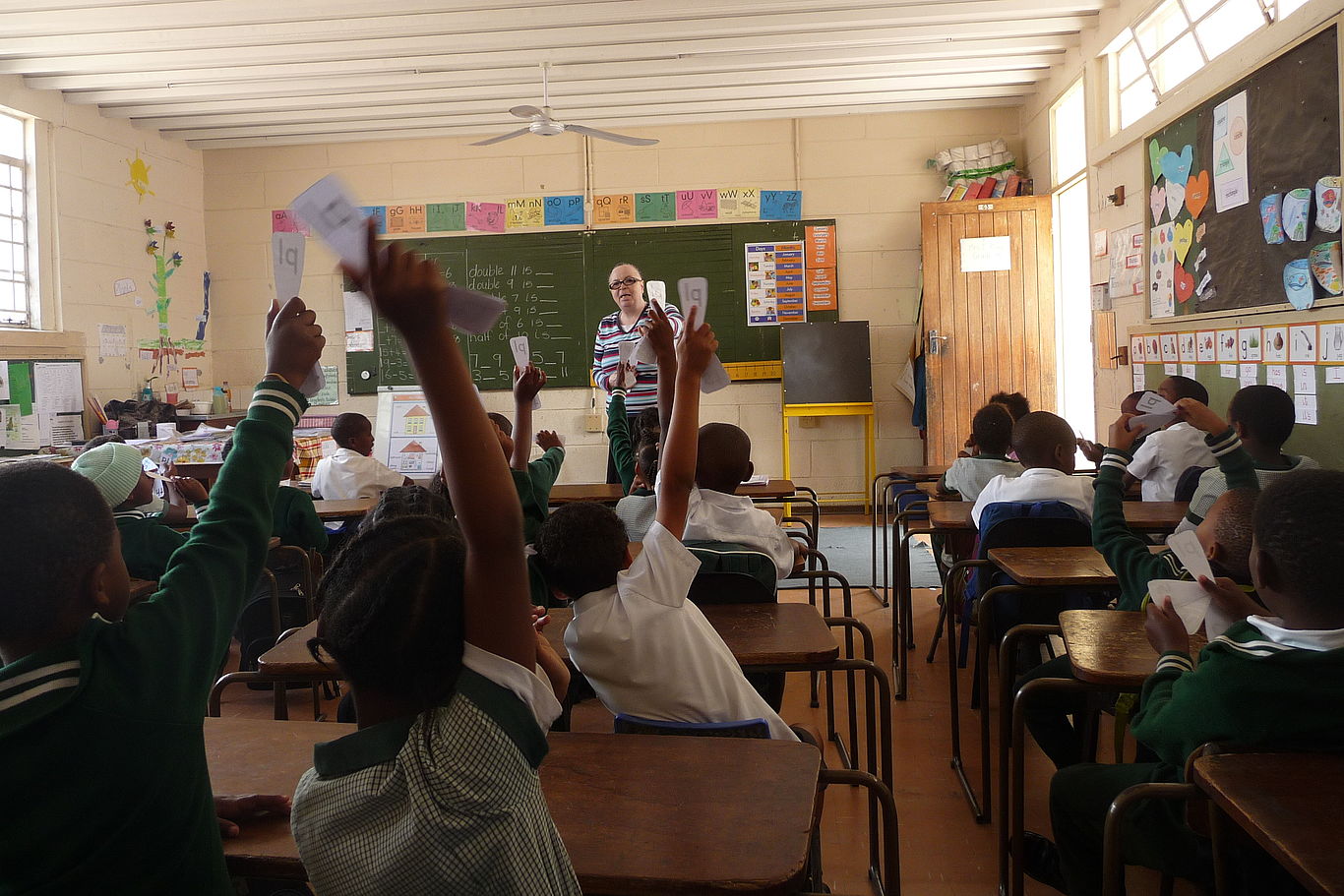 Engagierte Mitarbeit während des Unterrichts Kinder in einem Klassenzimmer von MCC zeigen auf.
