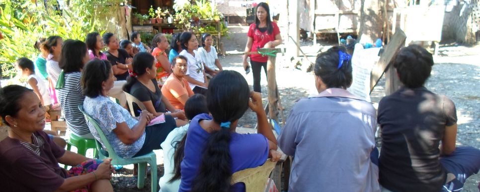 Einschulung einer Frauengruppe von CAM in Davao Eine Frauengruppe von CAM sitzt im Halbkreis im Freien und erhält eine Einschulung