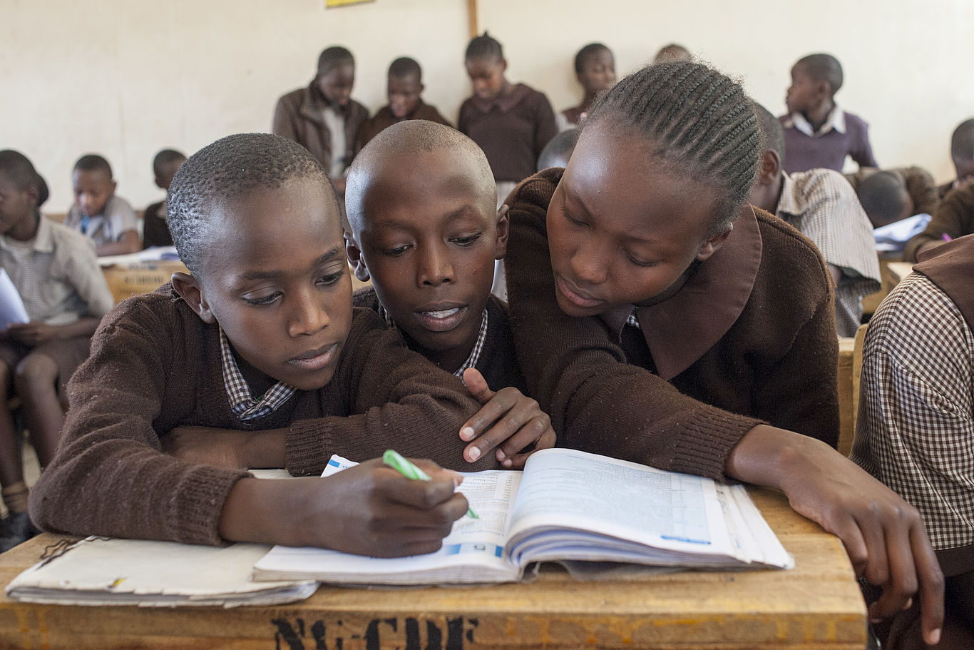 Drei Kinder beugen sich in einem Klassenzimmer über ihr Schulbuch.