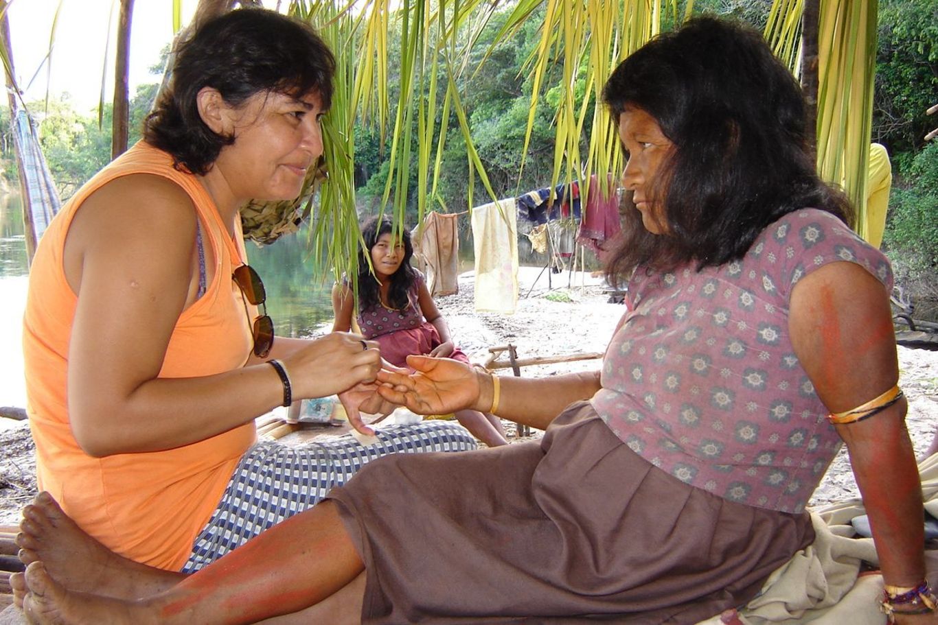 Eine indigene Frau berührt die Hand einer anderen und blickt ihr tief in die Augen