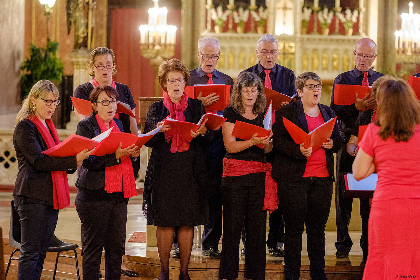 Mehrere Personen in schwarz-roter Kleidung singen gemeinsam als Chor.