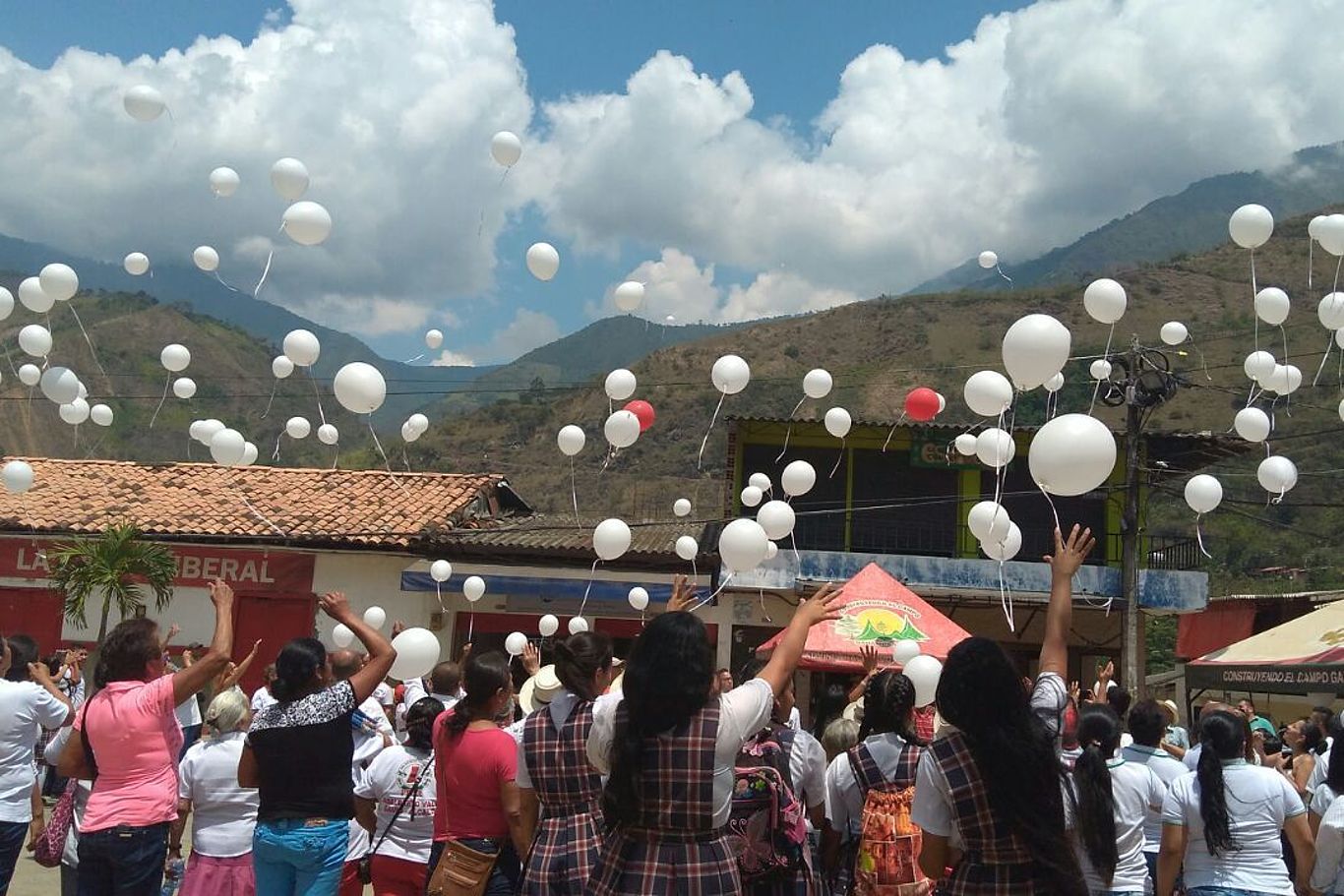 Viele Menschen stehen vor einer Häuserreihe und lassen weiße Luftballons steigen