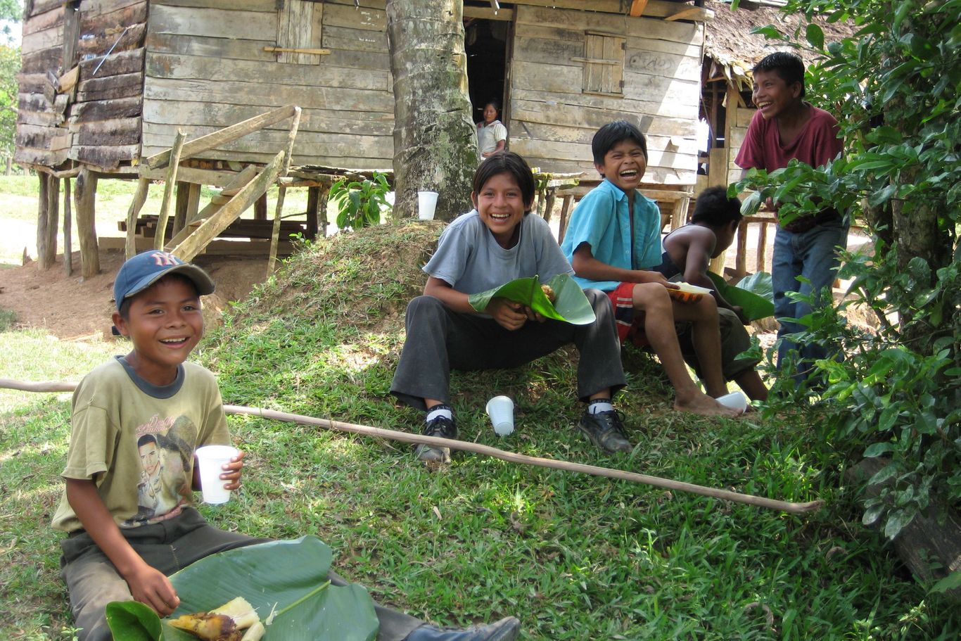 Vier Kinder sitzen im Gras, essen und trinken und lächeln in die Kamera