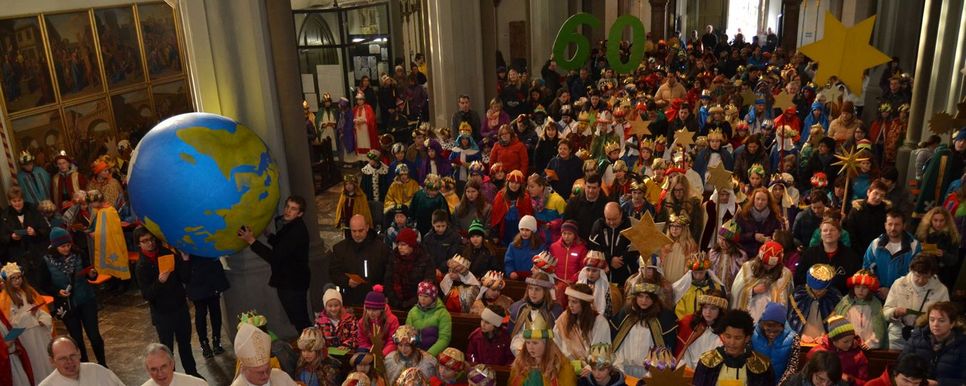 Viele, als Sternsinger/innen verkleidete Kinder sitzen mit ihren Familien in einer Kirche und es wird ein Weltkugel Ball hochgehalten