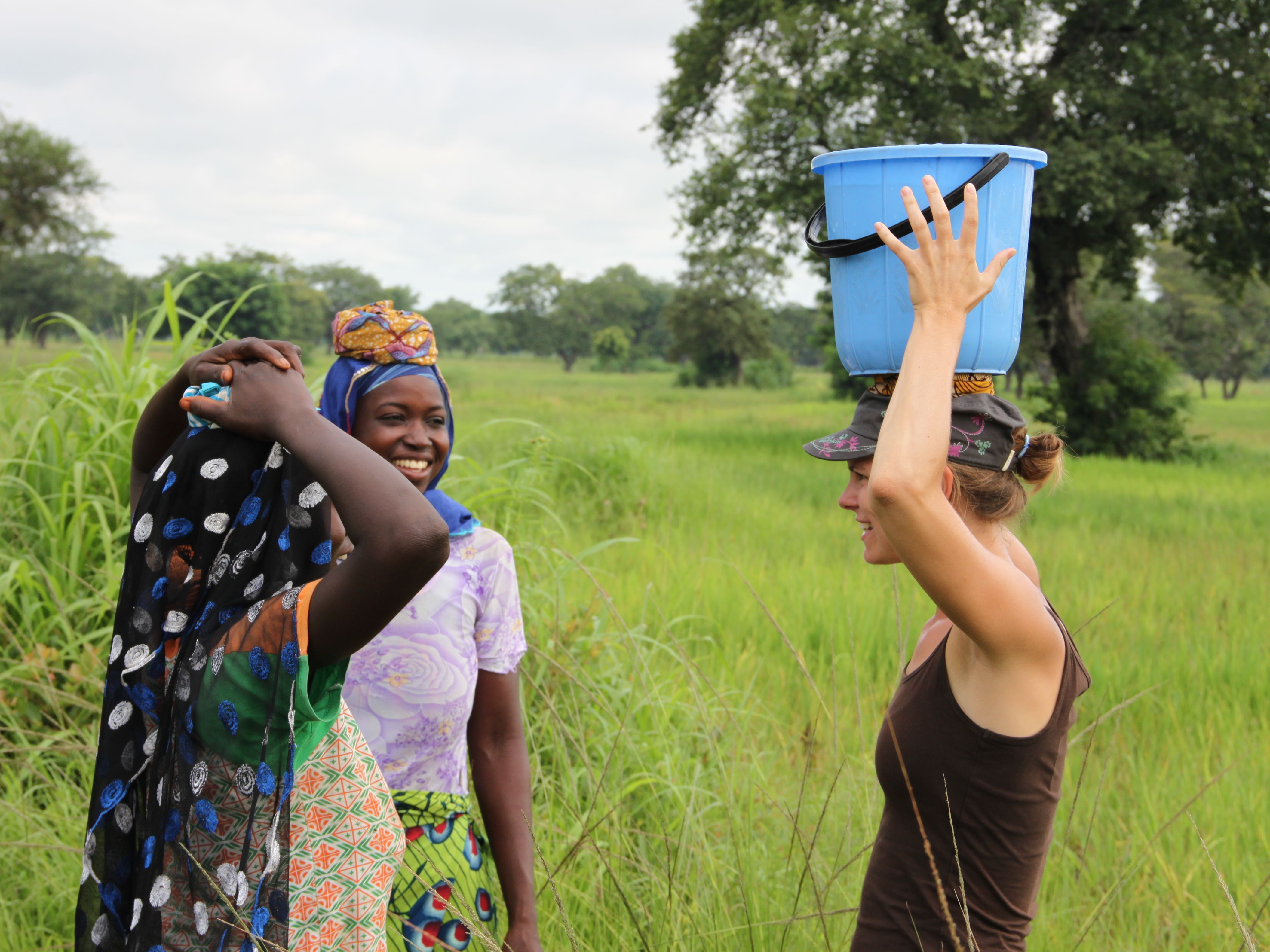 Frauen aus Ghana und Österreicherin unterhalten sich. Allte tragen Eimer auf dem Kopf. 