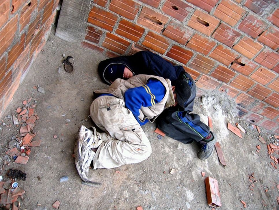 Zwei Kinder liegen in Schlafsäcke gewickelt auf der Straße