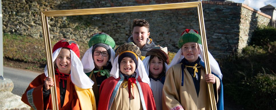 Sternsinger/innen verlautbaren weihnachtliche Friedensbotschaft. Sternsingerkinder halten einen goldenen Rahmen und lächeln.