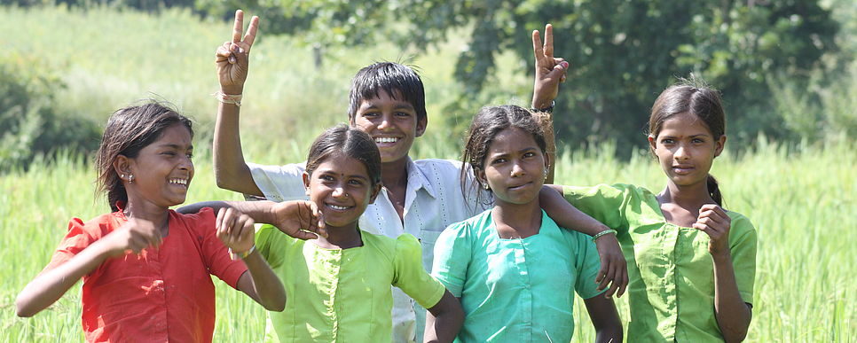 Kinder stehen in einem Reisfeld und lächeln in die Kamera