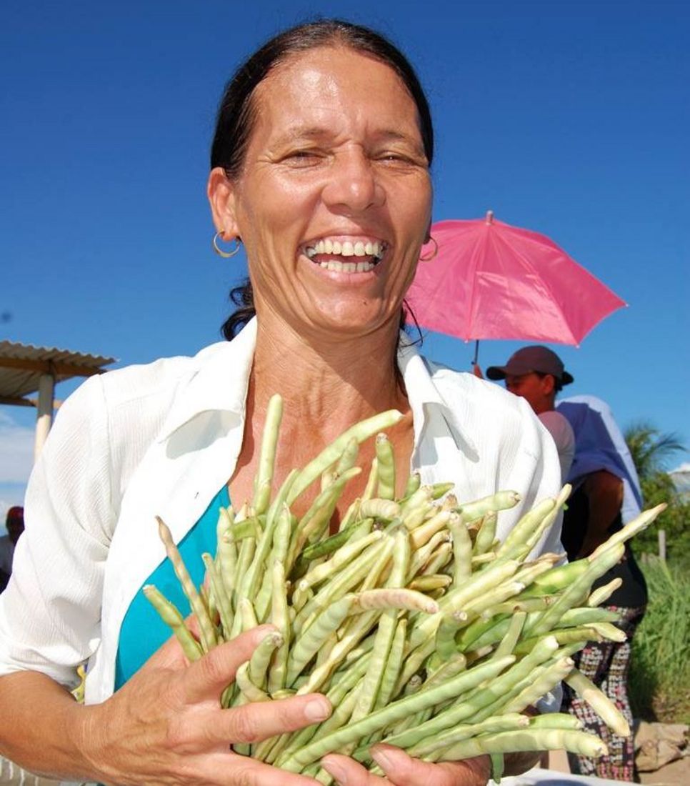 Eine Frau hält eine Hand voll Bohnen und lächelt in die Kamera.