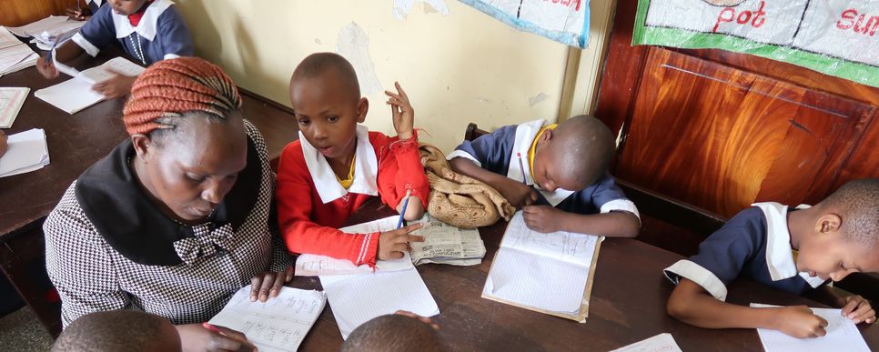 Kinder aus Nairobi sitzen mit einer Lehrerin auf einem Tisch und machen Schulaufgaben.