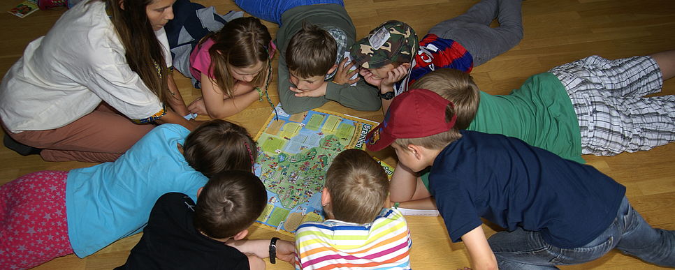 Einige Kinder liegen im Kreis und studieren eine bunte Landkarte