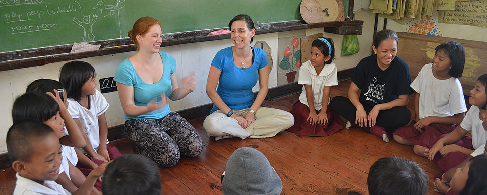 Eine Gruppe philippinischer Kinder sitzen mit zwei Teilnehmerinnen im Kreis und unterhalten sich.