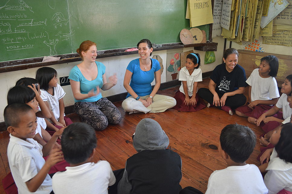 LernEinsätzler und philippinische Kinder sitzen im Kreis und unterhalten sich.