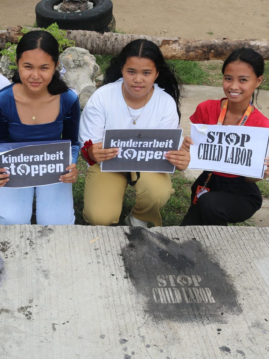 Mehrere Jugendliche und junge Erwachsene knien am Boden hinter Reverse Graffiti mit der Schrift "Kinderarbeit stoppen".