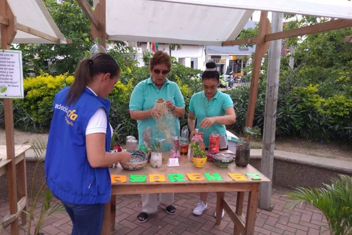 Personen stehen an einem Verkaufsstand und präsentieren verschiedene Pflanzen in kreativen Töpfen.