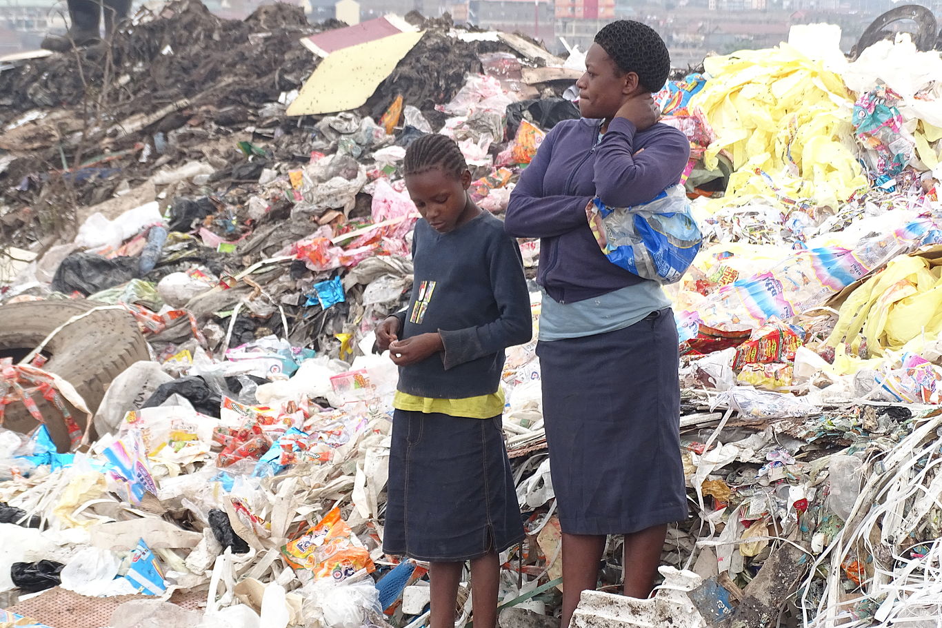 Eine Frau und ein Mädchen stehen vor einer Mülldeponie.