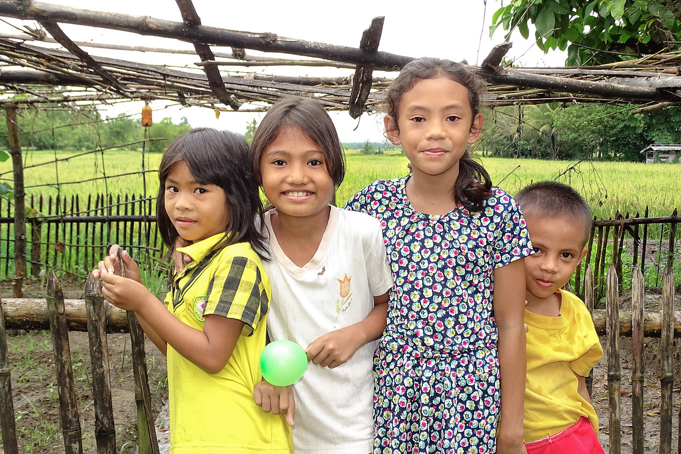 Vier Kinder stehen vor einem Zaun und lächeln in die Kamera.