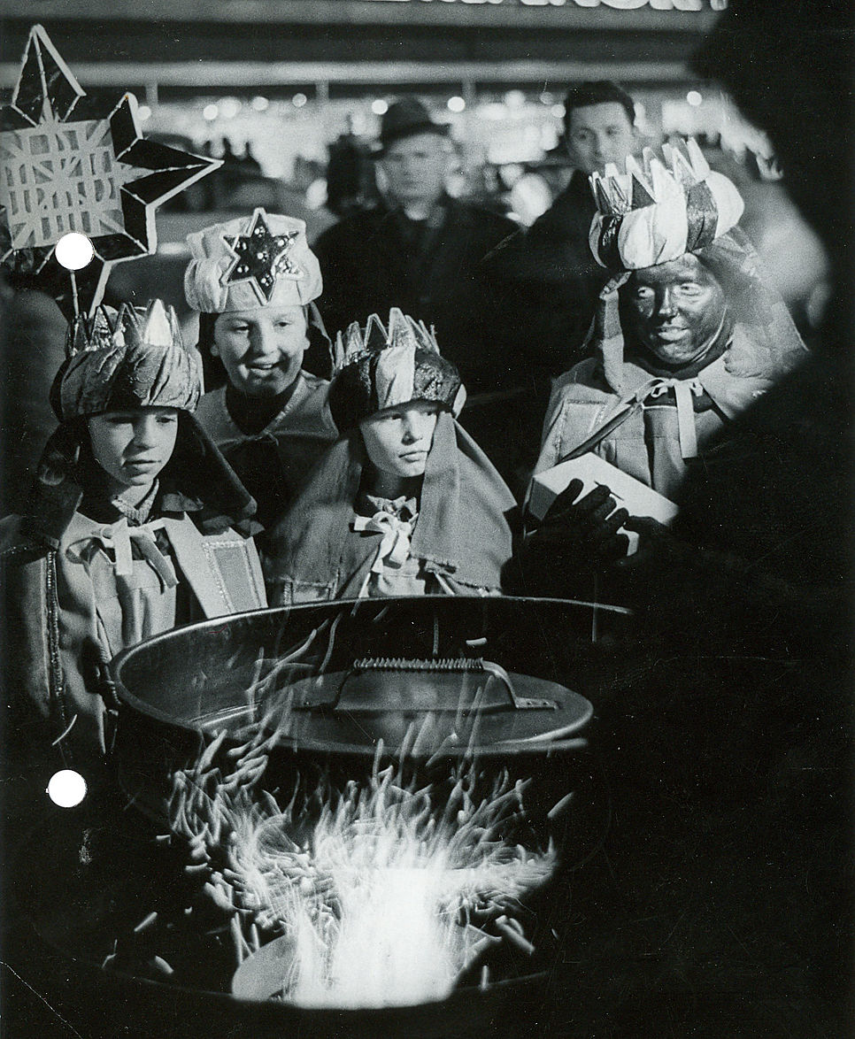 Vier Stersinger/innen stehen vor einem Maroniofen in dem ein Feuer brennt.